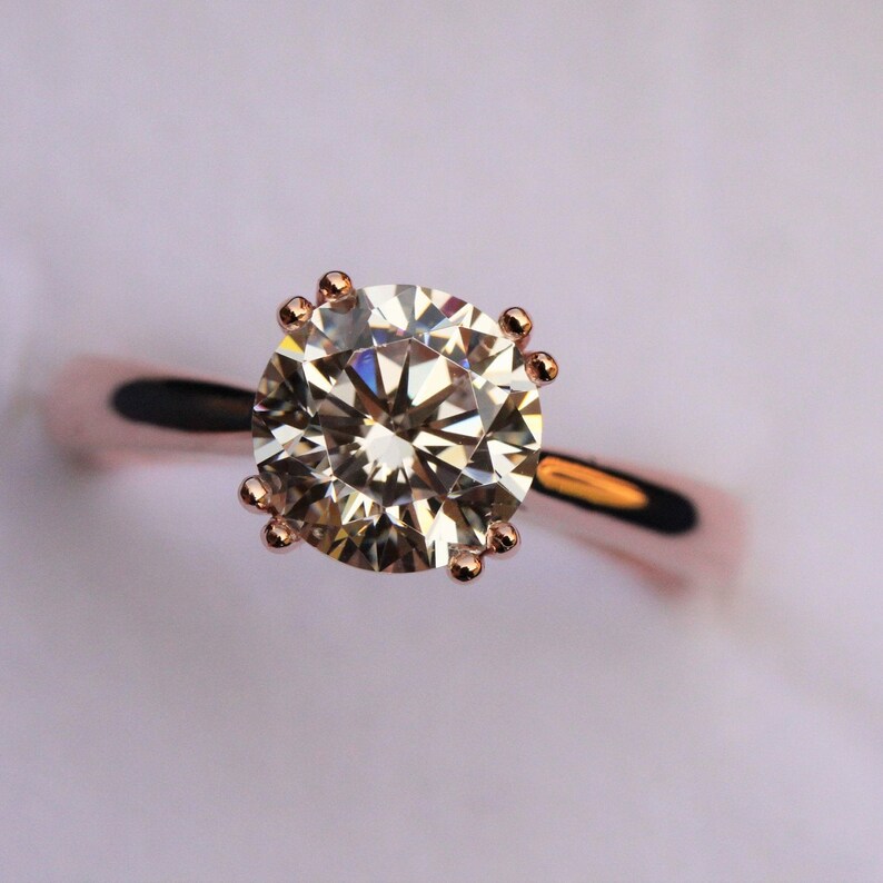 May include: A rose gold engagement ring with a large, round, clear diamond.