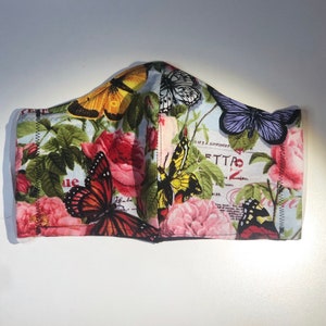 May include: A face mask with a floral print featuring butterflies and roses. The fabric is white with a light blue background. The mask has a sewn seam around the edges.
