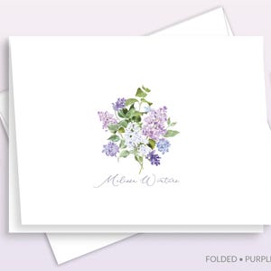 May include: A white folded stationery card featuring a watercolor illustration of purple and white lilac flowers with green leaves. The name Melissa Winters is printed in a thin, black script font below the floral arrangement.