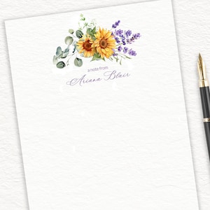 May include: A white notepad with a floral design featuring sunflowers and lavender. The text "a note from Ariana Blair" is printed in purple at the bottom of the notepad.