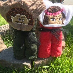 May include: Two hooded towels featuring embroidered character faces on the hoods. One towel is dark green with a brown-haired character hood, and the other is bright red with a white hood featuring a character wearing a pink floral crown.