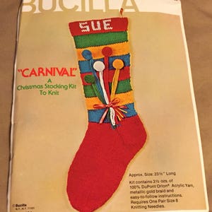 May include: A Bucilla "Carnival" Christmas stocking kit to knit, featuring a red stocking with a green, yellow, and blue striped pattern. The stocking has a white pom-pom and a red bow. The kit includes 3 1/2 ounces of 100% DuPont Orlon acrylic yarn, metallic gold braid, and easy-to-follow instructions. It requires one pair of size 8 knitting needles. The kit is 23 1/2 inches long.
