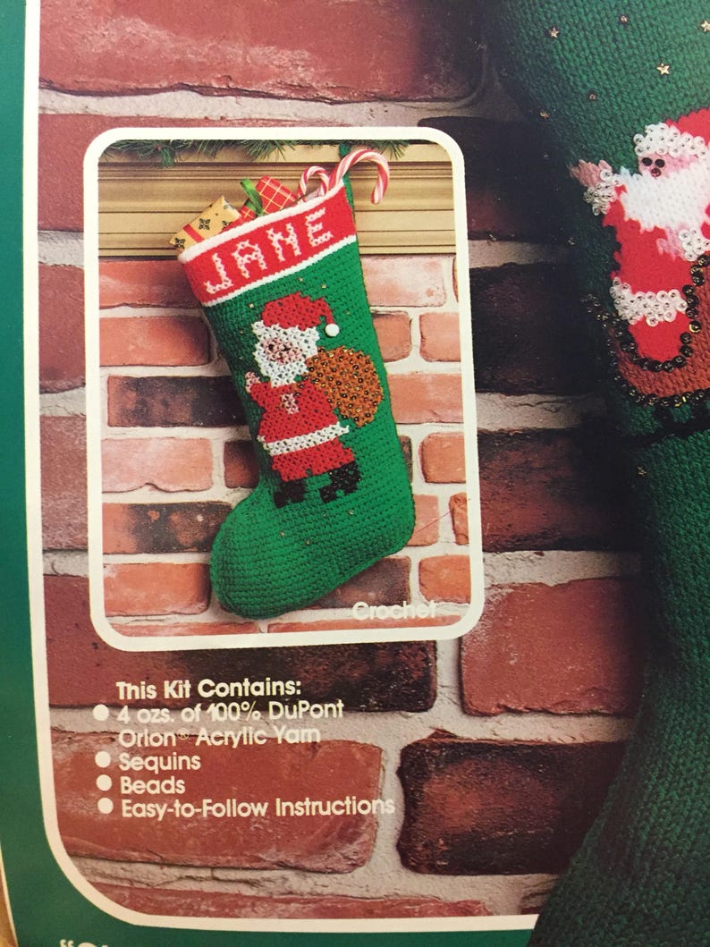 May include: A green and red crochet stocking with the name "JANE" embroidered on the front. The stocking features a Santa Claus figure holding a bag of gifts. The kit includes 4 ounces of 100% DuPont Orion Acrylic yarn, sequins, beads, and easy-to-follow instructions.