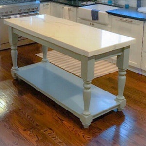 May include: A white kitchen island with a light blue base and a white countertop. The island has a lower shelf and turned legs.