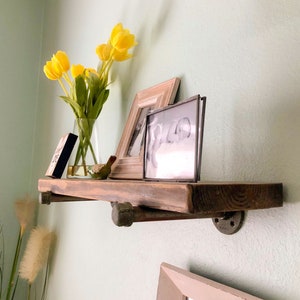 Puede incluir: Una estanter&iacute;a de madera r&uacute;stica con soportes de metal negro, que presenta un jarr&oacute;n de tulipanes amarillos, una foto en blanco y negro enmarcada y una foto en color enmarcada. La estanter&iacute;a est&aacute; montada en una pared de color verde claro.
