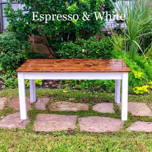 Puede incluir: Una mesa de madera con una base blanca y una tapa marr&oacute;n. La mesa est&aacute; te&ntilde;ida de color espresso y tiene un acabado brillante. La mesa est&aacute; situada en un camino de piedra en una zona de c&eacute;sped.