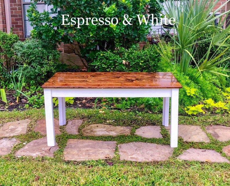 Puede incluir: Una mesa de madera con una base blanca y una tapa marr&oacute;n. La mesa est&aacute; te&ntilde;ida de color espresso y tiene un acabado brillante. La mesa est&aacute; situada en un camino de piedra en una zona de c&eacute;sped.