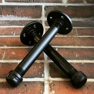 Puede incluir: Dos soportes de estante de tuber&iacute;a de metal negro con bridas. Los soportes est&aacute;n cruzados entre s&iacute;.
