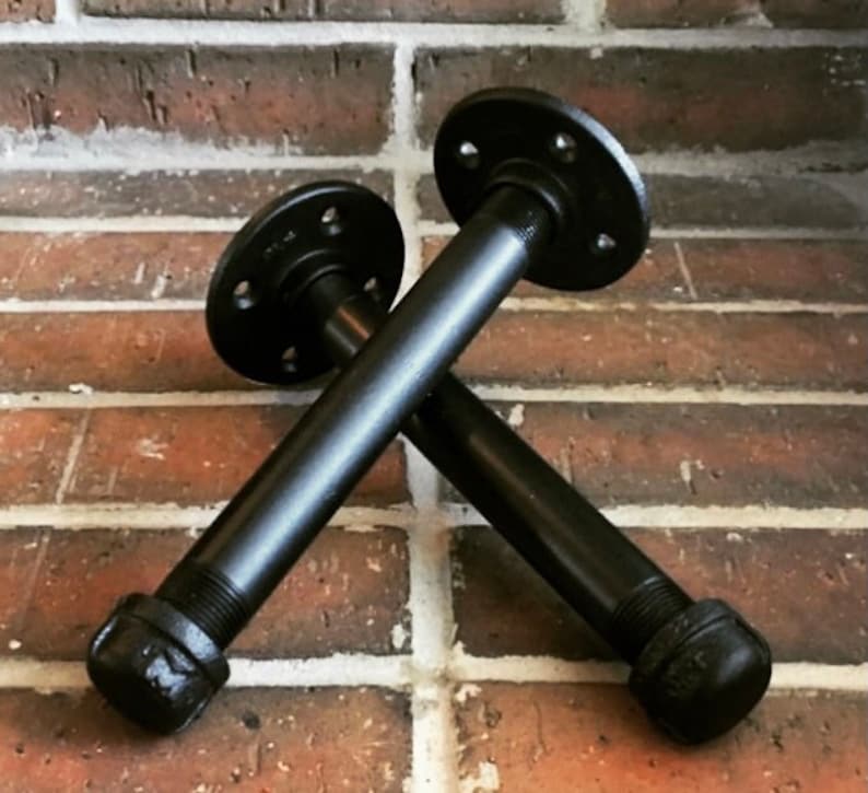 Puede incluir: Dos soportes de estante de tuber&iacute;a de metal negro con bridas. Los soportes est&aacute;n cruzados entre s&iacute;.