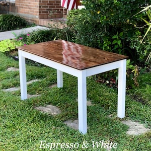Puede incluir: Una mesa de madera con una tapa de madera te&ntilde;ida de color espresso marr&oacute;n oscuro y patas pintadas de blanco. La mesa est&aacute; sentada en un c&eacute;sped.