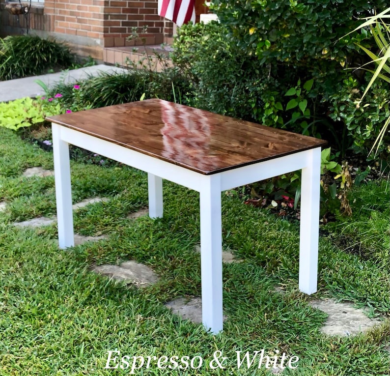 Puede incluir: Una mesa de madera con una tapa de madera te&ntilde;ida de color espresso marr&oacute;n oscuro y patas pintadas de blanco. La mesa est&aacute; sentada en un c&eacute;sped.
