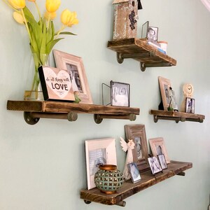 Puede incluir: Cuatro estantes de madera r&uacute;stica con soportes de tuber&iacute;a met&aacute;lica, decorados con fotos enmarcadas, una peque&ntilde;a casita de p&aacute;jaros, una placa decorativa en forma de coraz&oacute;n que dice "do all things with love" y una peque&ntilde;a figurita de &aacute;ngel decorativa.