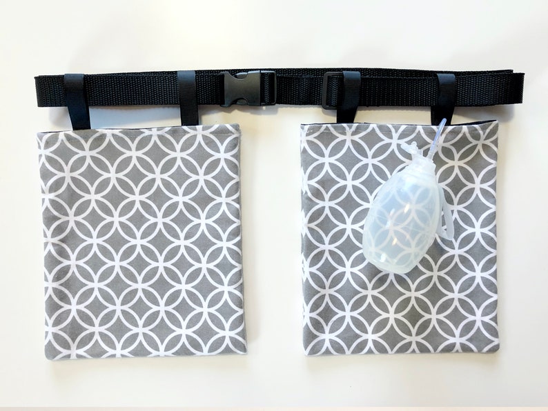 Puede incluir: Un cintur&oacute;n negro ajustable de nailon con hebilla de pl&aacute;stico que cuenta con dos bolsas rectangulares de tela gris con un patr&oacute;n de c&iacute;rculos blancos entrelazados. Una peque&ntilde;a pera de goma transparente con un tubo fino est&aacute; sujeta a una bolsa.