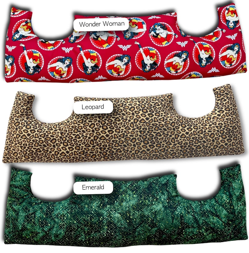 May include: Three neck pillows with different patterns. The top pillow is red with Wonder Woman graphics. The middle pillow has a leopard print. The bottom pillow is emerald green with a textured pattern. Each pillow has a unique shape.