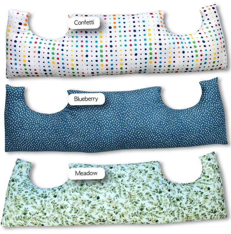 May include: Three long, curved pillows with cut-out sections. The top pillow has a white background with colourful polka dots. The middle pillow is navy blue with white dots. The bottom pillow has a light blue background with green leaf patterns. Each pillow has a label.