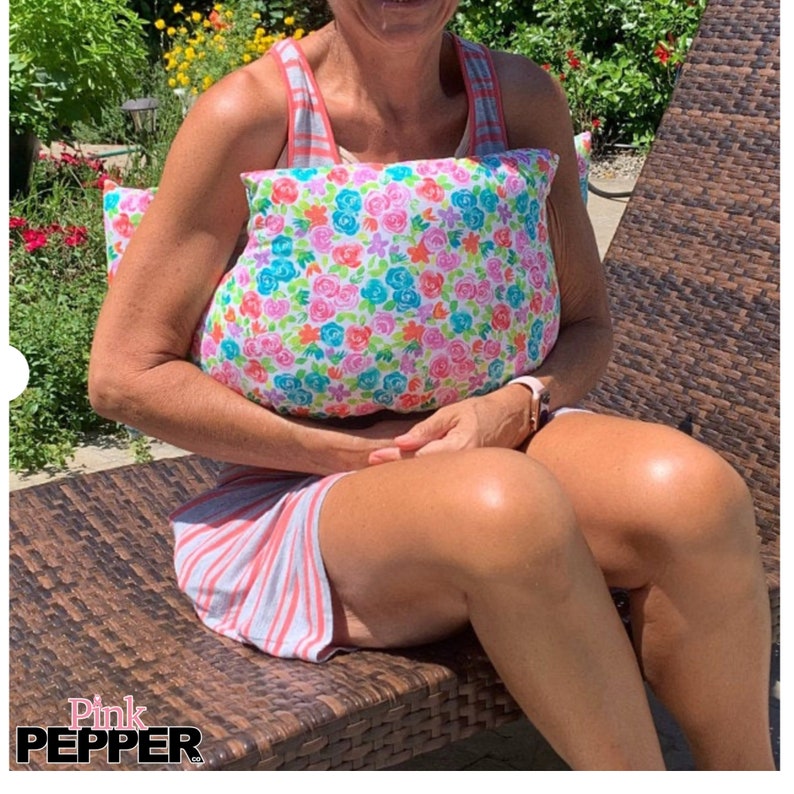 May include: A rectangular pillow featuring a floral pattern with pink, blue, and orange flowers on a white base. The pillow is likely cotton. The text "Pink Pepper" is visible in the bottom left corner.