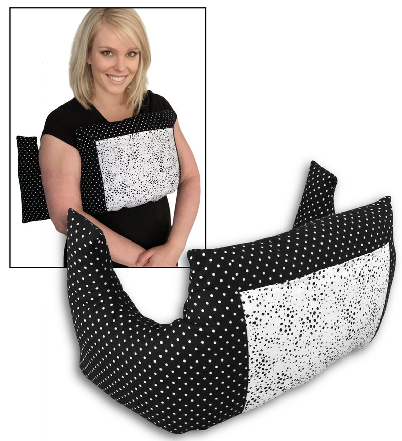 May include: A black and white polka dot pillow with a white square panel. The pillow is designed to be worn around the neck and shoulders. An additional smaller pillow is also visible. The design is a mix of polka dots and a white, speckled pattern.