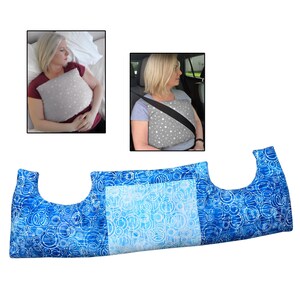 May include: A blue and white patterned pillow with a unique shape, designed for comfort. The pillow is shown in use in a car and while sleeping. The pillow has a light blue centre and a blue and white circular pattern on the sides.