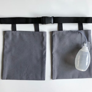 Puede incluir: Un soporte de tela gris para bolsas de drenaje m&eacute;dico con un cintur&oacute;n negro ajustable y hebilla de pl&aacute;stico. Dos bolsas rectangulares grises est&aacute;n unidas al cintur&oacute;n mediante correas negras. Una pera de drenaje m&eacute;dica transparente est&aacute; unida.