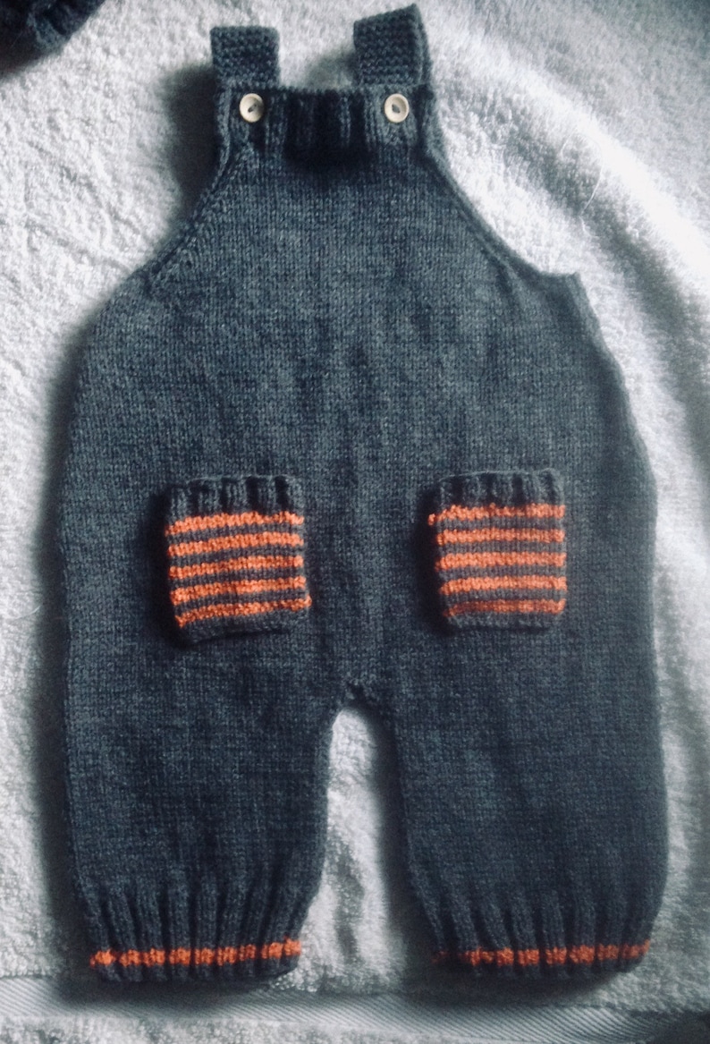 Hand knitted baby dungarees with striped patch pockets detail with over shoulder wooden fastenings also available with matching cardigan.