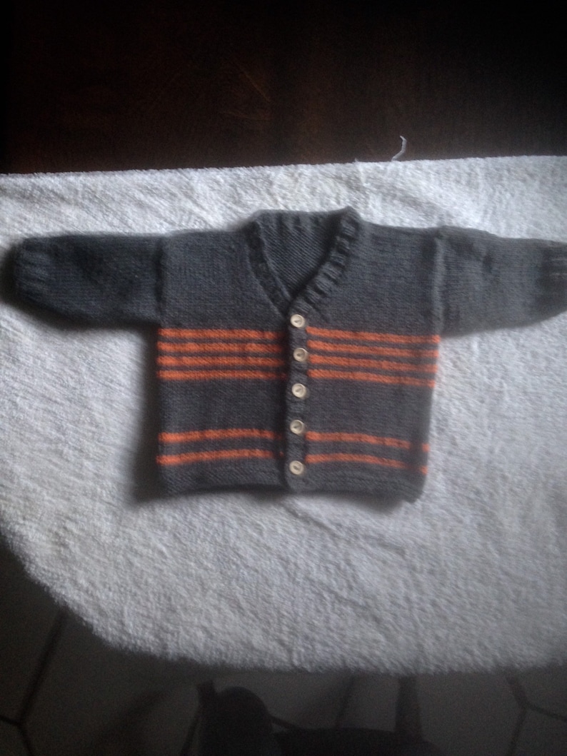 Hand knitted baby dungarees with striped patch pockets detail with over shoulder wooden fastenings also available with matching cardigan.