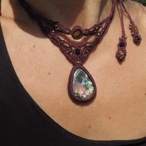 May include: A maroon macrame necklace with a teardrop-shaped iridescent labradorite gemstone pendant. The necklace features smaller tiger's eye and black beads.