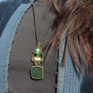 Può includere: Una donna indossa una giacca di jeans blu con una collana con ciondolo in pietra verde e turchese. La collana è realizzata in macramè e ha una pietra di forma quadrata al centro.