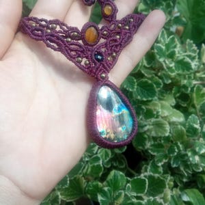 May include: A handmade macrame necklace with a large iridescent labradorite gemstone pendant. The necklace is made with burgundy cord and features smaller tiger's eye and black onyx beads.