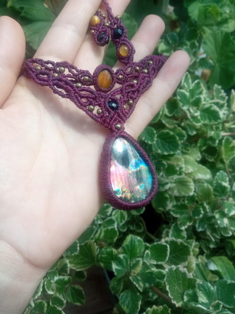 May include: A handmade macrame necklace with a large iridescent labradorite gemstone pendant. The necklace is made with burgundy cord and features smaller tiger's eye and black onyx beads.