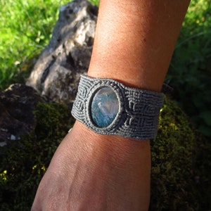 May include: Gray macrame bracelet with a blue and white agate stone in the center.