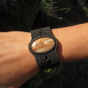 May include: A black macrame bracelet with a brown and white agate stone in the center.