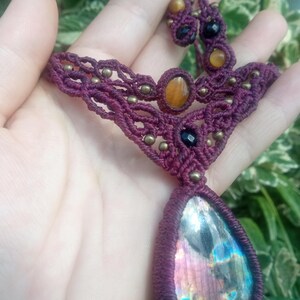 May include: A maroon macrame necklace with a large iridescent labradorite gemstone pendant. The necklace also features smaller tiger's eye and black onyx beads.