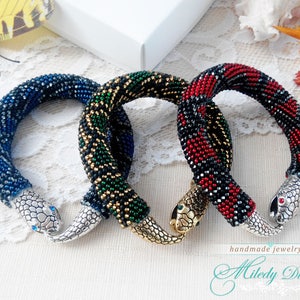 Puede incluir: Tres pulseras de serpiente de cuentas con cierres de cabeza de serpiente plateados. Las pulseras son azules, verdes y rojas con detalles negros.