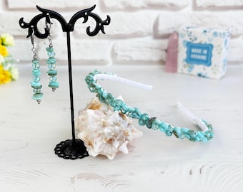 May include: A pair of dangling earrings featuring light blue stone chips on silver-toned hooks, displayed on a black stand, alongside a matching headband adorned with similar light blue stone chips on a white band.