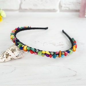 May include: A black headband adorned with a dense arrangement of small, multi-colored stone chips in shades of red, yellow, green, blue, and purple, interspersed with tiny metallic beads along the entire length of the thin, flexible frame.