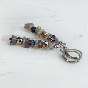 May include: A pair of dangle earrings featuring a mix of gray, gold, and blue beads. The earrings have a lever-back closure and are displayed on a white surface. The beads are of varying sizes and shapes.