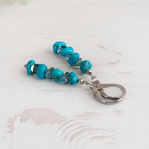 May include: A pair of drop earrings featuring bright turquoise stone chips and small iridescent glass beads strung on silver-toned metal wire, finished with secure silver-toned leverback closures for attachment to the earlobe.