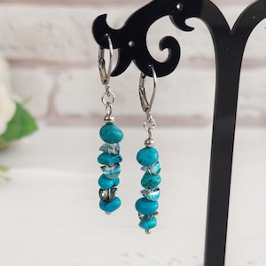 May include: Dangling earrings with turquoise and clear beads. The earrings are made of silver-colored metal and feature a lever-back closure. The turquoise beads are a vibrant blue-green color, and the clear beads add a touch of sparkle.
