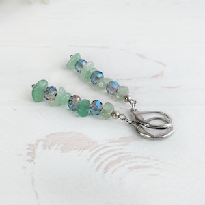 May include: A pair of drop earrings featuring silver-toned leverback fastenings. Each earring is composed of alternating light green stone chips and faceted, iridescent blue-grey glass beads arranged in a vertical line on a metal wire.