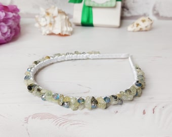 May include: A white headband embellished with a series of small, light green and blue faceted stones. The stones are arranged in a continuous row along the top of the band, creating a textured surface with a subtle shimmer.