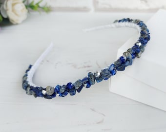 May include: A thin headband wrapped in white material and adorned with a dense arrangement of small, irregular, deep blue lapis lazuli stone chips interspersed with tiny, reflective silver-toned metallic beads throughout the band.