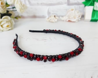 May include: A thin headband featuring a black base adorned with a dense arrangement of small, dark black beads interspersed with vibrant, round red beads. The accessory has a textured, beaded surface that covers the entire outer curve of the band.