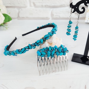 Könnte beinhalten: Ein Haarschmuck-Set bestehend aus einem schwarzen Haarreif und einem silberfarbenen Haarkamm, beide verziert mit kleinen, unregelmäßigen türkisfarbenen Steinen und klaren Perlen. Ein Paar passende Ohrhänger hängt an einem schwarzen Ständer.