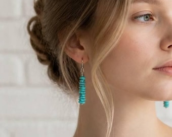May include: Dangle earrings featuring a vertical stack of small, cylindrical turquoise beads in a vibrant blue-green hue. The beads are strung on a thin silver-toned metal wire, creating a simple, elongated drop design that hangs from the earlobe.
