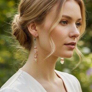 May include: Dangle earrings featuring a vertical arrangement of small, round, pale pink beads and clear, faceted crystal accents suspended from silver-toned hooks. The earrings hang delicately, showcasing a light-reflecting design with alternating bead textures and soft, neutral color tones.