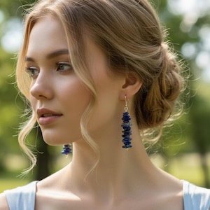 May include: Dangle earrings featuring a vertical stack of small, irregular, deep blue lapis lazuli gemstone chips suspended from silver-toned metal hooks. The earrings hang straight down, showcasing the natural texture and rich color of the stones.