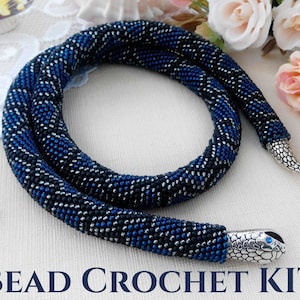 Può includere: Una lunga e flessibile collana a corda realizzata all'uncinetto con perline, caratterizzata da un motivo ripetuto di perline nero opaco, blu metallizzato e argento. Le estremità presentano teste di serpente in metallo argentato.