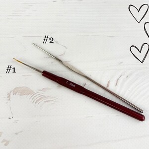 May include: Two crochet hooks, one silver and one red, labelled #1 and #2. The red hook is labelled 1.0mm.