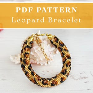 May include: A beaded bracelet featuring a leopard print pattern in shades of gold, brown, and black. The bracelet has gold-toned metal end caps and a gold-toned chain extender with a lobster clasp. The text PDF PATTERN Leopard Bracelet is visible.