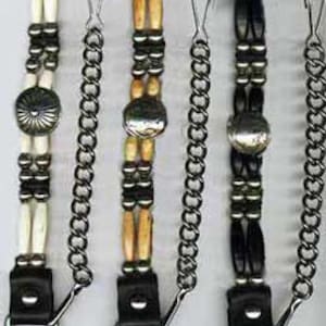 Puede incluir: Tres llaveros de moto de cuero negro con cuentas de hueso y metal, un dije plateado y una cadena de metal.